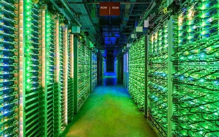 The blinking lights of racks of Google servers glow in a darkened data hall in St. Ghislain, Belgium.