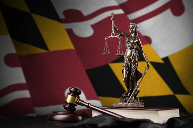 Maryland State Flag behind Lady Justice figurine and gavel.
